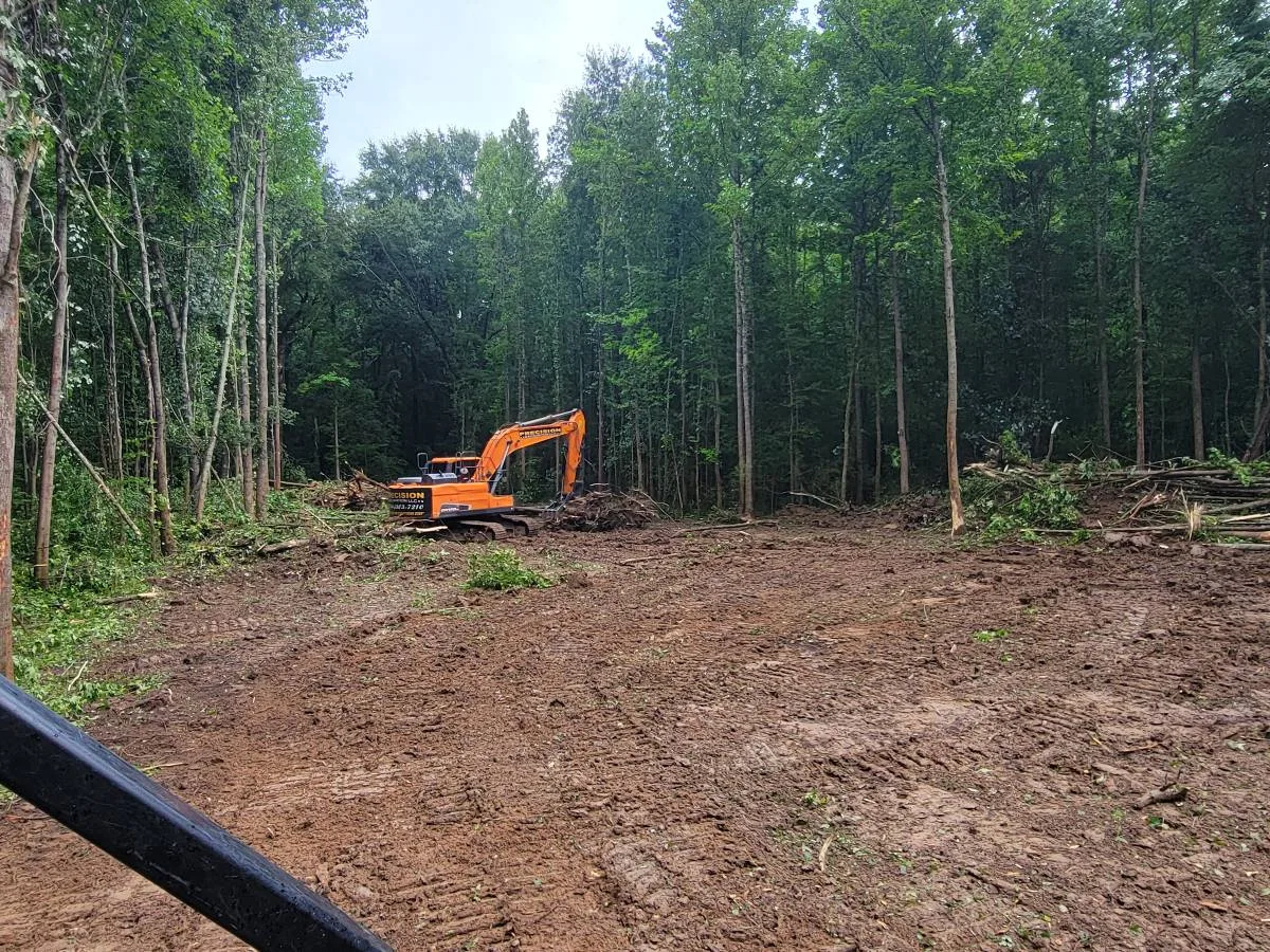 Trackhoe working through a wooded tract with the ground opened up to bare dirt